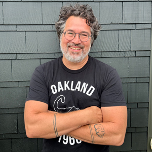 Tomas Moniz, a smiliing Latino man with glasses and a beard